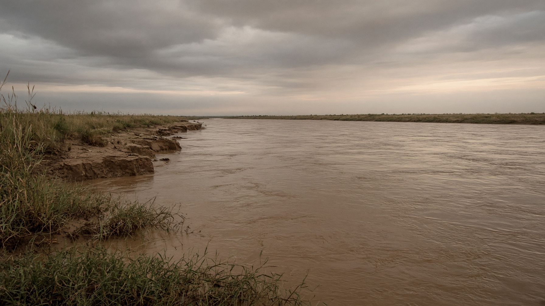 A wide brown river at dusk, silt banks and reed, no temple and no name planted.